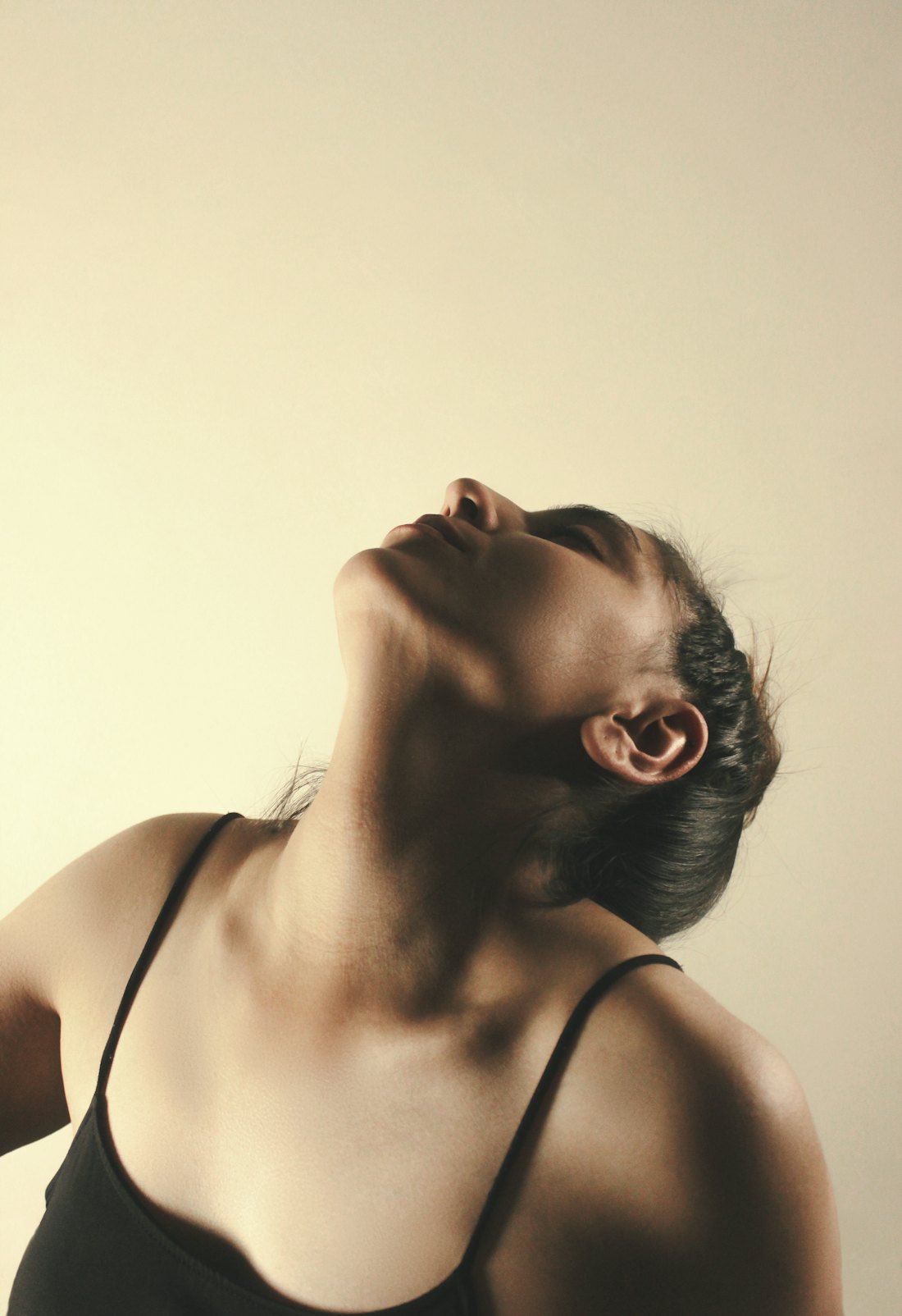 Woman tilting her head back slowly in soft warm light against a plain cream background