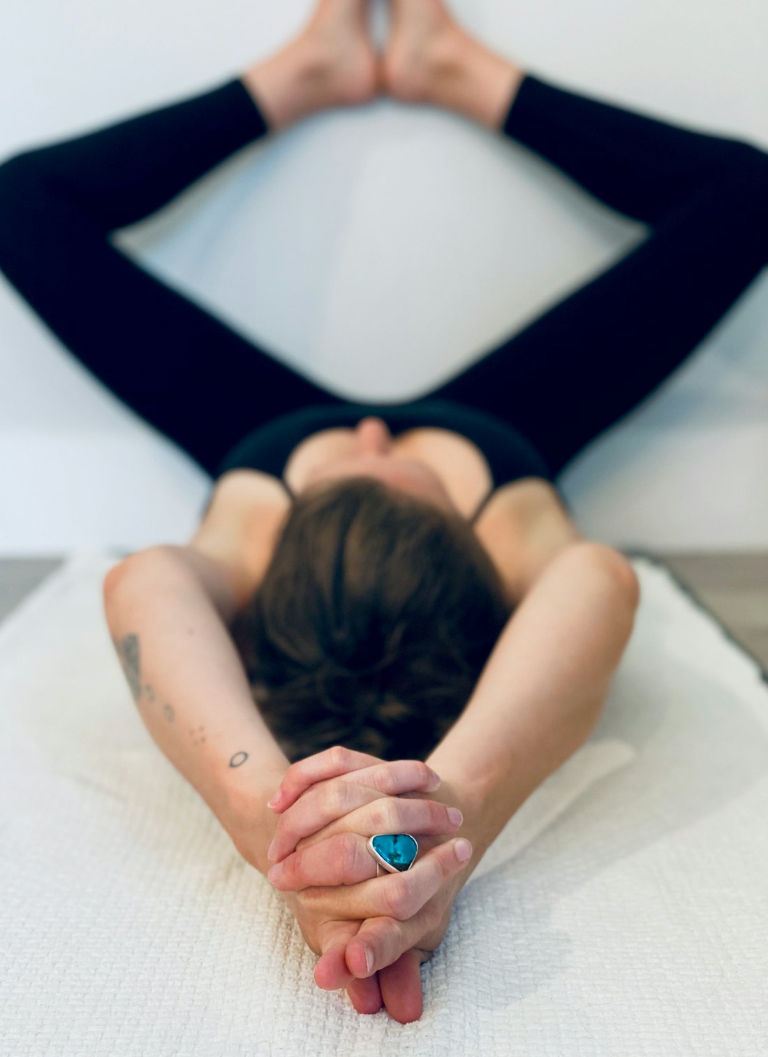 Person lying on a white bed with legs resting up against a wall and hands loosely clasped, in a relaxed position