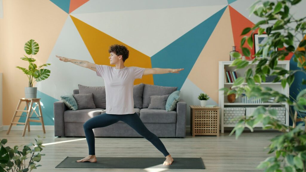 Woman holding a warrior two pose on a mat in a living room with a colourful geometric wall
