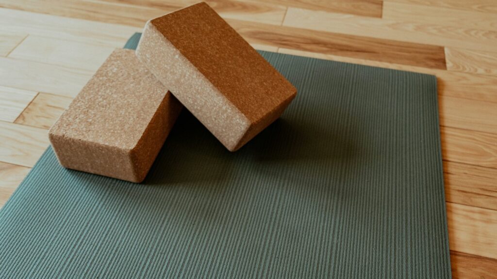 Olive green exercise mat on a light wooden floor with two cork blocks resting on top