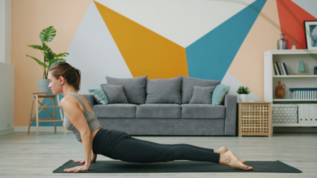 Woman lifting her chest in a gentle back bend on a mat in a living room with a colourful geometric wall