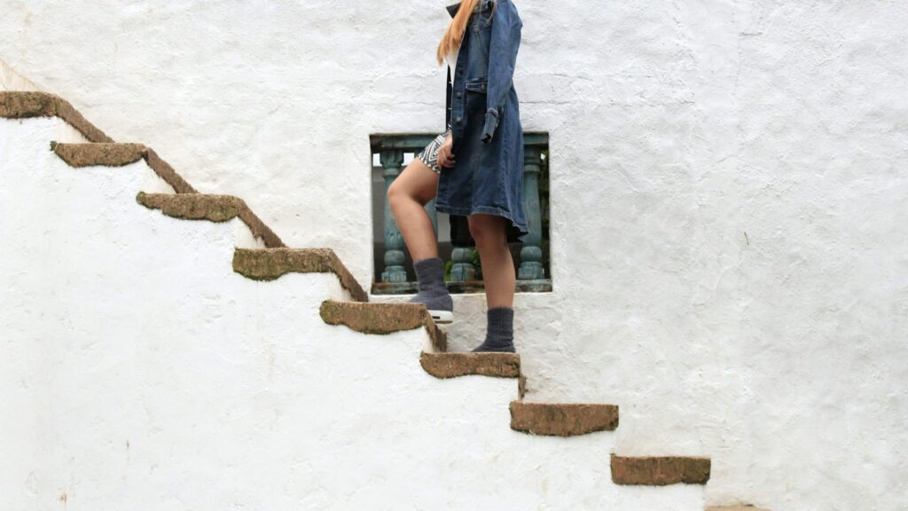 Woman in a denim jacket walking up an outdoor staircase set into a white wall